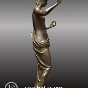 May include: A bronze sculpture of a woman standing with her arms raised, holding a small object in each hand. The woman is wearing a flowing robe and has a serene expression on her face.