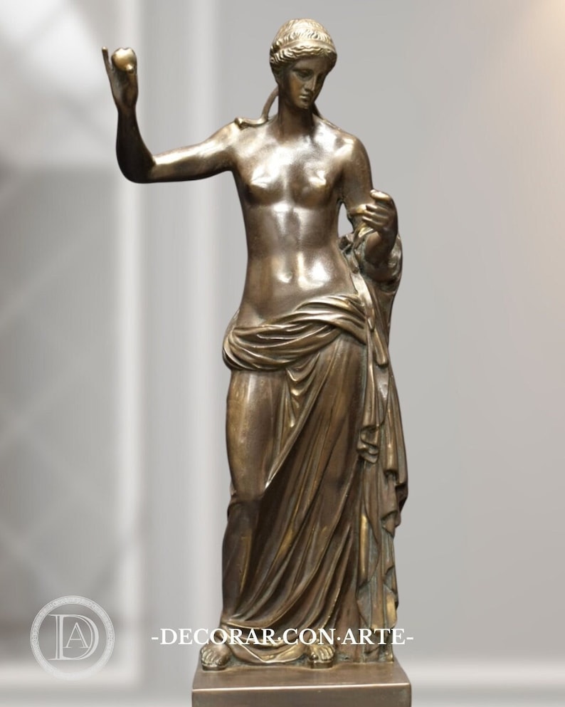 May include: A bronze sculpture of a woman standing with her arms outstretched, wearing a flowing robe. The sculpture is on a square base.