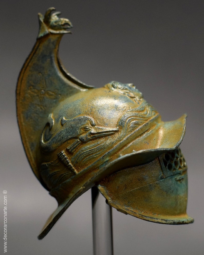 May include: A bronze helmet with a dolphin design and a face mask. The helmet has a tall, pointed crest and a decorative design on the side.