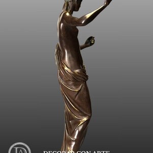 May include: Bronze sculpture of a woman standing on a base. She is wearing a flowing robe and holding a small object in her right hand. The sculpture is in a classic style.