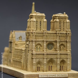 May include: A detailed miniature replica of the Notre Dame Cathedral in Paris, France. The model is made of a light brown material and features intricate details, including the two iconic towers, the rose window, and the main entrance.