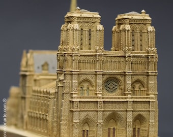 May include: A detailed miniature replica of the Notre Dame Cathedral in Paris, France. The model is made of a light brown material and features intricate details, including the two iconic towers, the rose window, and the main entrance.