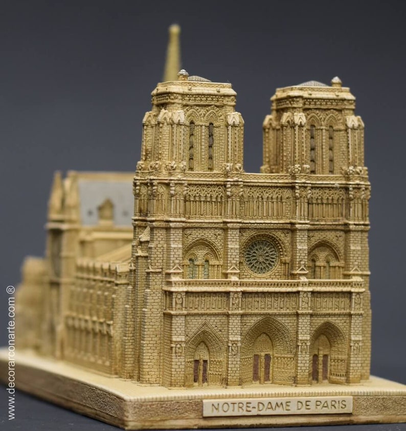 May include: A detailed miniature replica of the Notre Dame Cathedral in Paris, France. The model is made of a light brown material and features intricate details, including the two iconic towers, the rose window, and the main entrance.