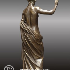 May include: Bronze sculpture of a woman standing with a flowing drapery. The sculpture is in a classical style and depicts a woman with her arm raised.