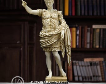 May include: A cream-colored statue of a Roman emperor, standing on a black base. The statue is detailed with armor and draped fabric, with one arm raised and pointing. The background features a dark bookshelf.