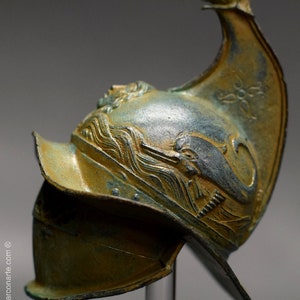 May include: A bronze helmet with a dolphin design and a pointed crest. The helmet is decorated with a wave pattern and has a green patina.