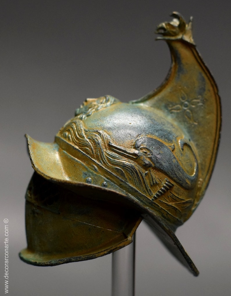May include: A bronze helmet with a dolphin design and a pointed crest. The helmet is decorated with a wave pattern and has a green patina.