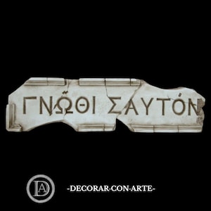 May include: A rectangular, off-white stone fragment with the Greek inscription "ΓΝΩΘΙ ΣΑΥΤΟΝ" carved into it. The fragment has a weathered appearance, with visible cracks and imperfections. The background is black.