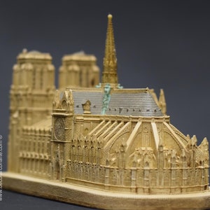 May include: A detailed miniature replica of the Notre Dame Cathedral in Paris, France. The model is made of a light brown material and features intricate details, including the iconic spire and gargoyles.