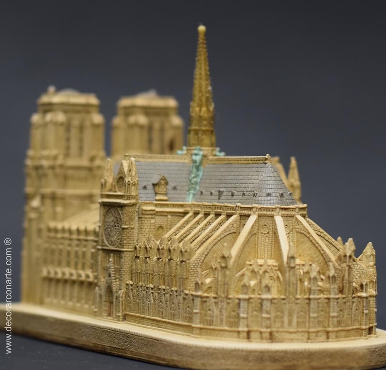 May include: A detailed miniature replica of the Notre Dame Cathedral in Paris, France. The model is made of a light brown material and features intricate details, including the iconic spire and gargoyles.