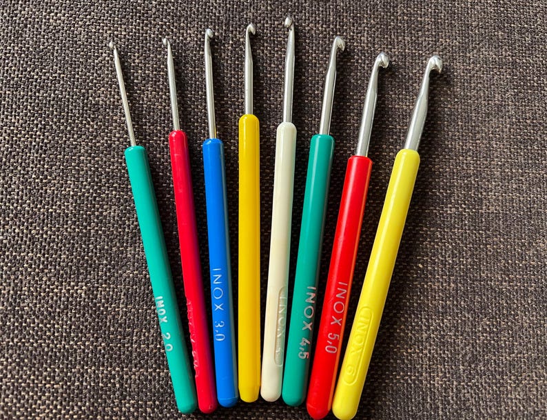 May include: A set of eight colorful crochet hooks with metal tips. The hooks are labeled with the size and brand "INOX".