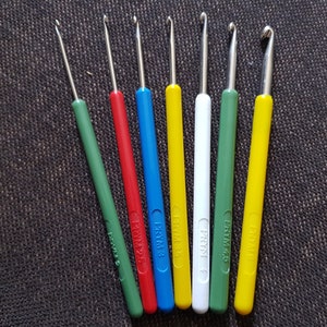 May include: A set of eight crochet hooks in various colors, including green, red, blue, yellow, and white. The hooks are labeled with the brand "FRYM" and the size number.
