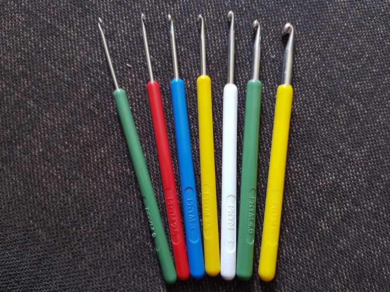 May include: A set of eight crochet hooks in various colors, including green, red, blue, yellow, and white. The hooks are labeled with the brand "FRYM" and the size number.