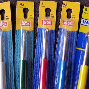 May include: Set of six crochet hooks in different sizes, ranging from 4 mm to 6 mm. The hooks are made of metal and have colorful plastic handles. The packaging is labeled with the size of each hook and the brand name "INOX".