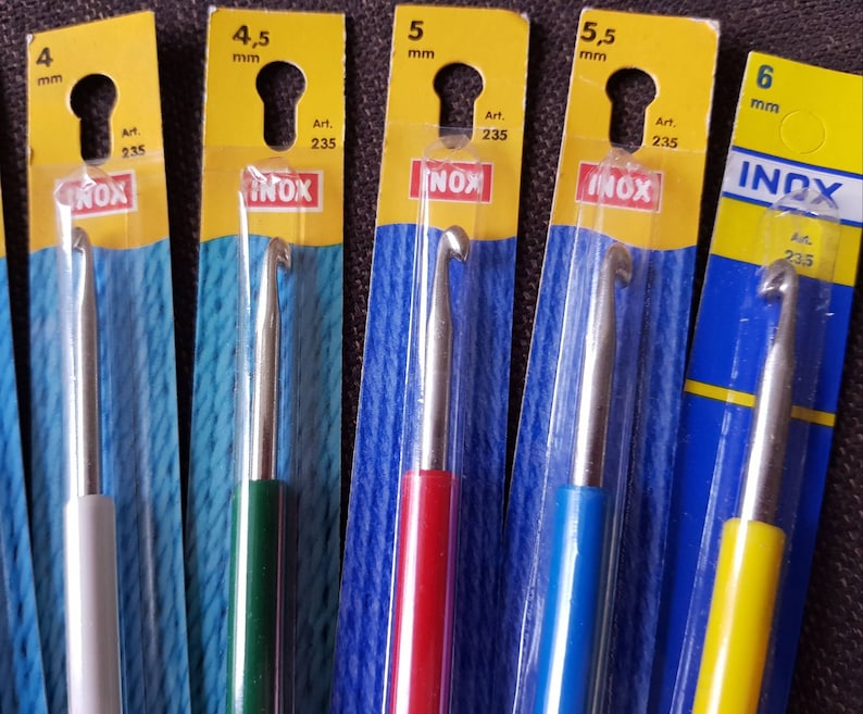 May include: Set of six crochet hooks in different sizes, ranging from 4 mm to 6 mm. The hooks are made of metal and have colorful plastic handles. The packaging is labeled with the size of each hook and the brand name "INOX".