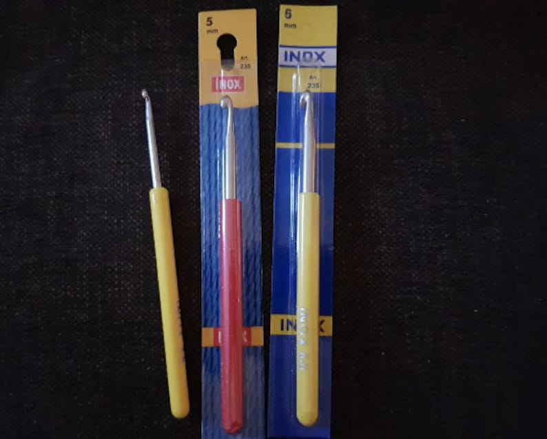May include: Three crochet hooks packaged in plastic. The hooks are 5 mm in size and are labeled "INOX". The hooks are yellow, red, and yellow.