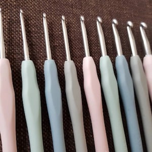 May include: A set of 12 crochet hooks in various sizes, with pink, green, and blue handles. The hooks are made of metal and have a smooth finish.