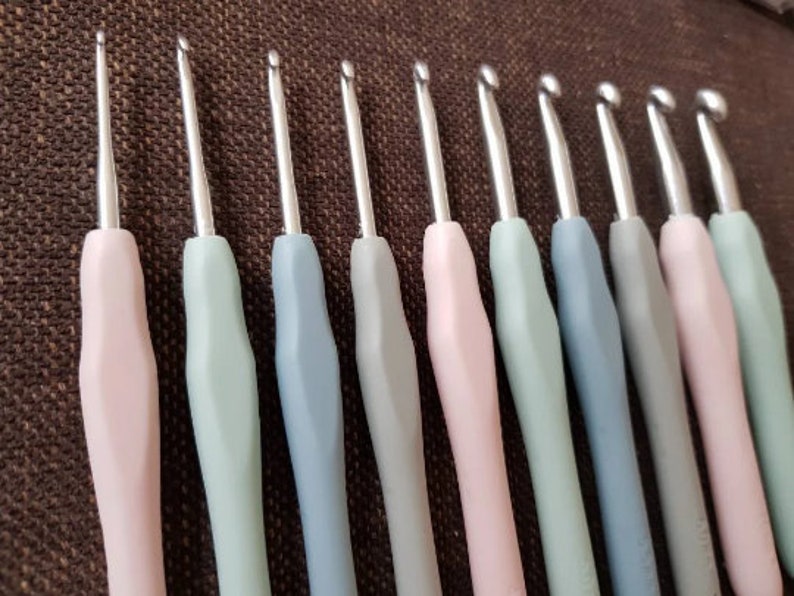 May include: A set of 12 crochet hooks in various sizes, with pink, green, and blue handles. The hooks are made of metal and have a smooth finish.
