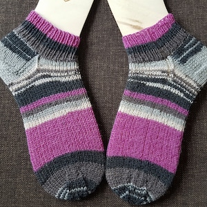 Könnte beinhalten: Ein Paar gestreifte Kniestrümpfe in den Farben Lila, Grau und Schwarz. Die Socken sind aus feinem Garn gestrickt und haben einen gerippten Bund.