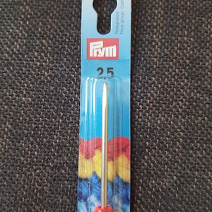 May include: A red and silver Prym crochet hook size 2.5 mm, packaged on a blue and yellow card with the text "Preisgruppe - Cat&eacute;gorie de prix - Price group" and "K" in a yellow circle.