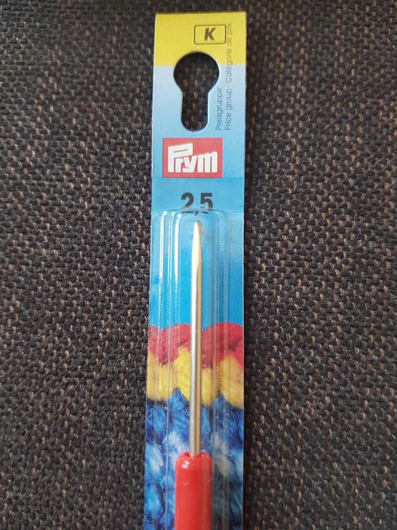 May include: A red and silver Prym crochet hook size 2.5 mm, packaged on a blue and yellow card with the text "Preisgruppe - Cat&eacute;gorie de prix - Price group" and "K" in a yellow circle.
