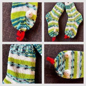 Könnte beinhalten: Handgestrickte Socken mit einem skurrilen Design. Die Socken weisen ein gestreiftes Muster in Grün-, Blau- und Weißtönen auf. Jede Socke hat ein rotes, klauenartiges Detail und kleine, weiße, strukturierte Verzierungen.