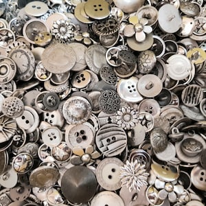 Könnte beinhalten: Eine große Sammlung von silbernen und grauen Knöpfen in verschiedenen Formen und Größen. Die Knöpfe sind aus Metall und haben eine Vielzahl von Designs, darunter Sterne, Blumen und geometrische Muster.