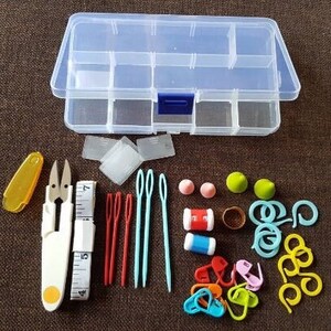 Könnte beinhalten: Eine transparente Plastik-Aufbewahrungsbox mit verschiedenen bunten Bastelutensilien, darunter Garn, Nadeln und Maschenmarkierer. Die Box hat mehrere Fächer zur Organisation von Kleinteilen.