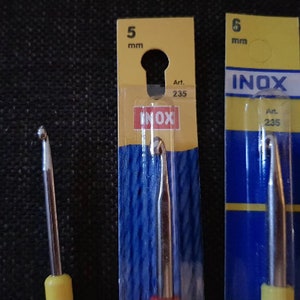 May include: Two crochet hooks, one 5 mm and one 6 mm, packaged in yellow and blue plastic packaging. The packaging has the word "INOX" printed on it. The hooks are made of metal and have yellow handles.