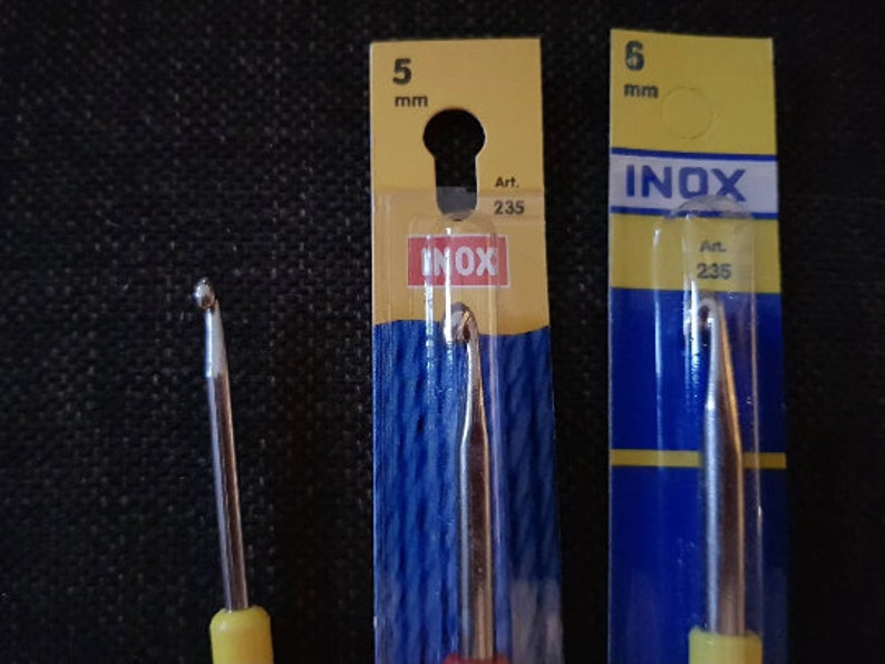 May include: Two crochet hooks, one 5 mm and one 6 mm, packaged in yellow and blue plastic packaging. The packaging has the word "INOX" printed on it. The hooks are made of metal and have yellow handles.