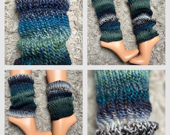 May include: Hand-knitted leg warmers in shades of blue, green, and gray. The leg warmers are displayed on a mannequin foot. The knitted texture is visible, with a ribbed cuff at the top and bottom. The yarn has a variegated color pattern.