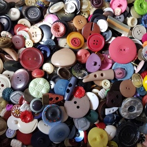 Könnte beinhalten: Eine große Sammlung von Vintage-Knöpfen in verschiedenen Farben, Formen und Größen. Die Knöpfe sind aus Kunststoff, Metall und Stoff. Einige der Knöpfe haben komplizierte Designs, während andere schlicht sind.