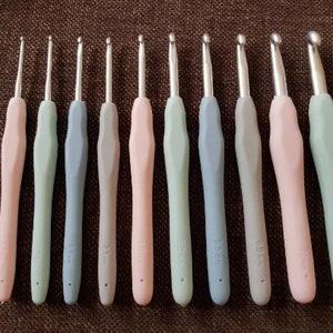May include: Set of ten crochet hooks in various sizes, ranging from 2.5 mm to 6.0 mm. The hooks are made of metal and have a colorful plastic handle. The handles are in shades of pink, blue, and green.