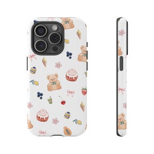 May include: White phone case featuring a repeating pattern of teddy bears, ice cream cones, pastries, berries, and lemons. The case has a glossy finish and a black border. The side view shows a slim profile with a pink flower accent.