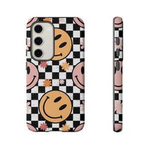 May include: A black phone case with a checkered pattern and smiling faces. The case has pink flowers and a cutout for the camera lens.