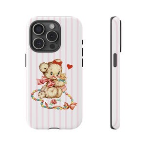 May include: A white phone case with a pink striped background. The case features a vintage illustration of a teddy bear with a pink bow, holding a doll, and a red heart. A colorful beaded necklace and a rose are also included in the design.