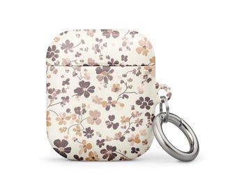 Puede incluir: Una funda blanca para AirPods con un estampado floral en tonos marrones y rosas. Tiene un anillo plateado para sujetar. La funda es cuadrada con bordes redondeados.