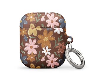 Puede incluir: Funda marrón para AirPods con un estampado floral en tonos rosa, amarillo, blanco y azul. Tiene un anillo metálico plateado para sujetar.
