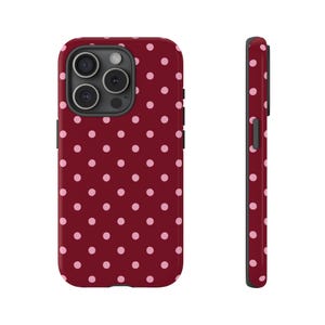May include: A burgundy phone case with a repeating pattern of pink polka dots. The case has a camera cutout and side buttons. The side view of the case shows the same polka dot pattern.
