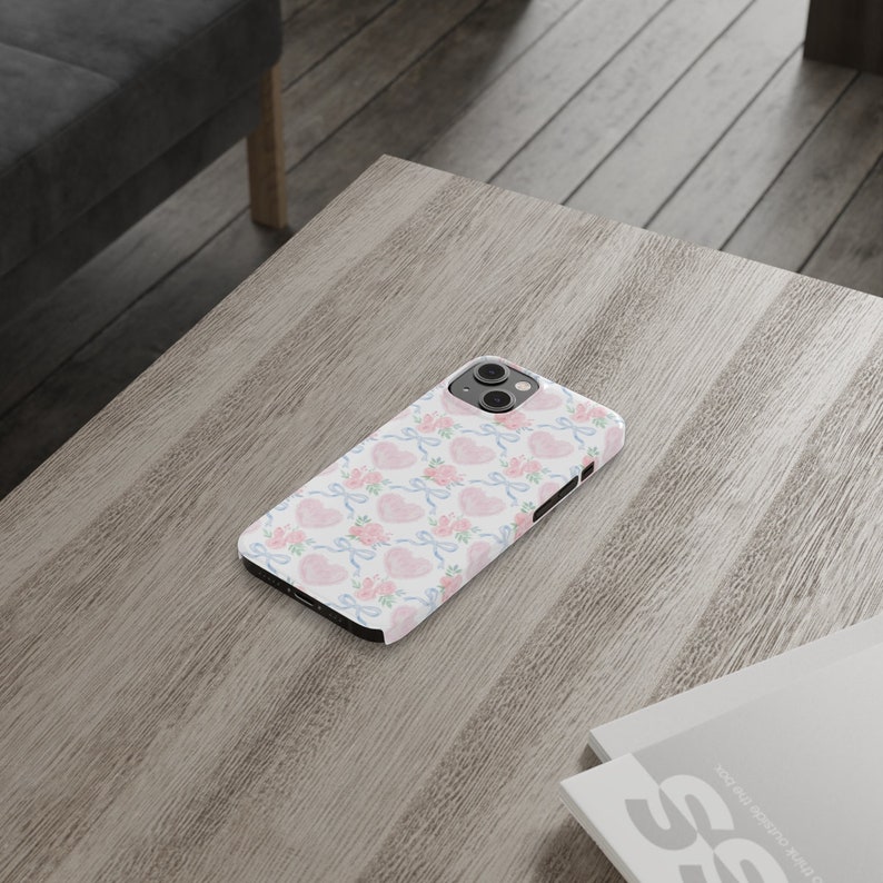 May include: A white phone case with a pink and blue watercolor pattern of hearts and bows.