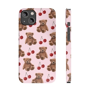 May include: A pink phone case with a repeating pattern of brown teddy bears and red cherries.
