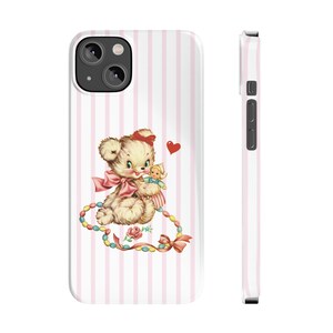 May include: A pink and white striped phone case with a cute cartoon teddy bear holding a doll. The teddy bear is wearing a pink bow and there is a red heart above it. The case has a colorful beaded necklace around the teddy bear.