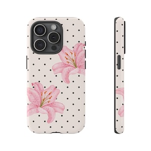 May include: A phone case featuring a cream background with black polka dots and pink watercolor lily flowers. The case has a camera cutout and side view showing the case's thickness.