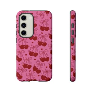 May include: Pink phone case with a pattern of red cherries and bows.