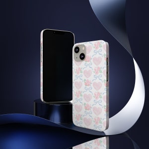 May include: A white phone case with a pink and blue watercolor pattern of hearts and bows. The case is designed for an iPhone.