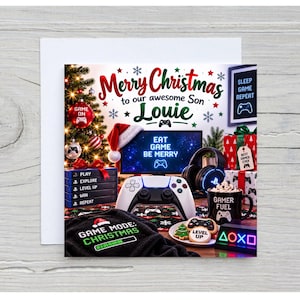 May include: A square Christmas greeting card featuring a gaming theme with a monitor displaying EAT GAME BE MERRY, a white controller, a black mug labeled GAMER FUEL, a stack of game cases, and a black shirt with GAME MODE: CHRISTMAS text.