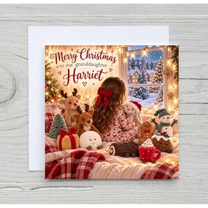 May include: A square Christmas greeting card featuring a child with long hair and a red bow sitting among plush toys, including reindeer, a snowman, and a gingerbread man. The text reads Merry Christmas to our granddaughter Harriet.