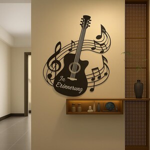 Könnte beinhalten: Schwarze Gitarrensilhouette mit Noten und dem Text "In Erinnerung" an einer Wand. Das Kunstwerk ist ein dekoratives Stück, wahrscheinlich für ein Musikzimmer oder einen Wohnraum. Das Design umfasst einen Violinschlüssel und andere musikalische Symbole.