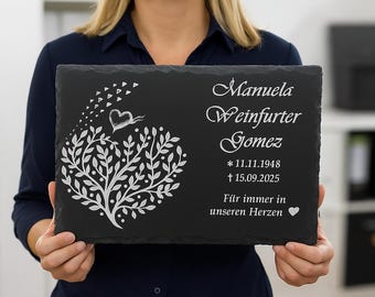 May include: A black slate memorial plaque with white engraved text and a tree design. The plaque includes a name, dates, and the phrase "Für immer in unseren Herzen".