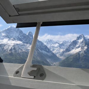 Könnte beinhalten: Ein Fensterrahmen mit einem weißen Stützarm und Blick auf schneebedeckte Berge unter blauem Himmel. Das Fenster ist teilweise geöffnet und bietet eine malerische Aussicht.